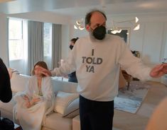 a man wearing a face mask while sitting on a couch with two other people in the background