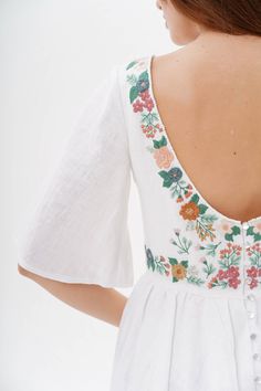 the back of a woman's white dress with flowers on it and buttons at the waist