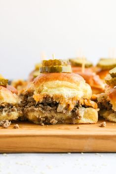 several sliders with pickles and cheese on them sitting on a wooden cutting board