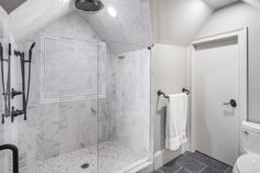 a white bathroom with black accents and marble tile flooring, along with a walk in shower