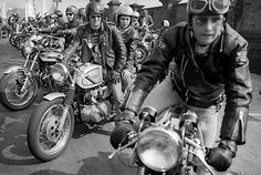 black and white photograph of men riding motorcycles on the street in front of other motorcyclists