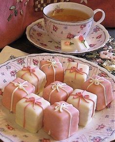 some pink and white treats on a plate with a cup of tea in the background