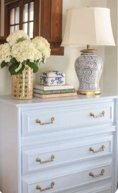 a blue and white dresser with flowers on it in front of a mirror, lamp and basket