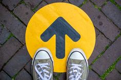 a pair of shoes standing on top of a yellow and black circular sign with an arrow