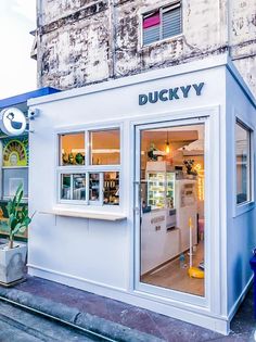 the outside of a small store called ducky, with its windows open and potted plants in front