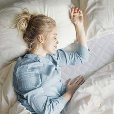 a woman is laying in bed with her arms up and looking at something on the pillow