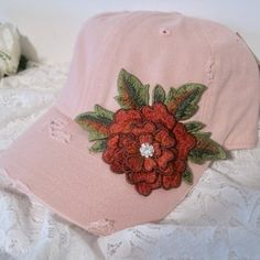 a pink baseball cap with red flowers on the front and side, sitting on white lace