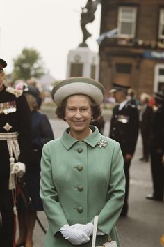 a woman in a green coat and hat standing next to other people on the street