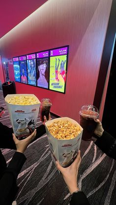 two people holding up buckets of popcorn in front of a screen with movies on it