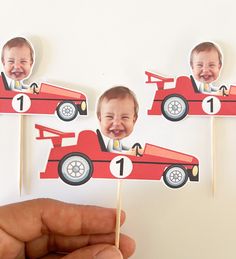 a hand holding up two cupcake toppers with pictures of babies in a race car