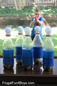 several bottles of water are lined up in front of a man holding an object with one hand