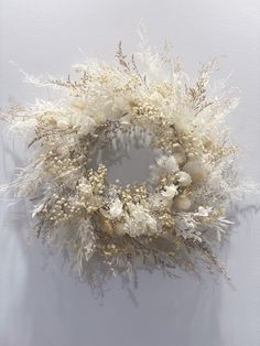 a white wreath hanging on the wall with dried flowers and leaves in it's center