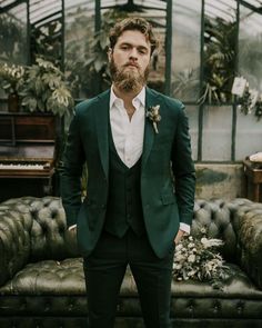 a man with a beard wearing a suit and bow tie standing in front of a couch