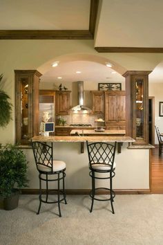 an open kitchen with two bar stools in the center and wooden cabinets on either side