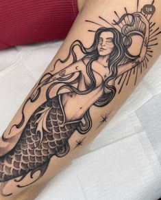 a woman with a tattoo on her arm is holding a sun above her head and mermaid tail