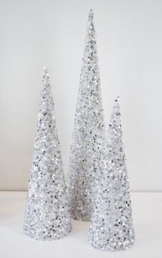 three silver glitter trees on a white surface