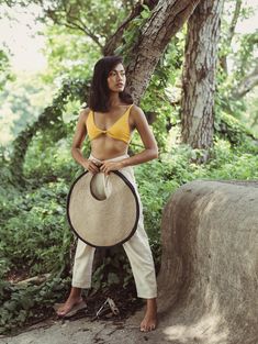 a woman standing in front of a tree holding a hat