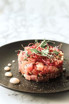 a black plate topped with meat and veggies on top of a white table