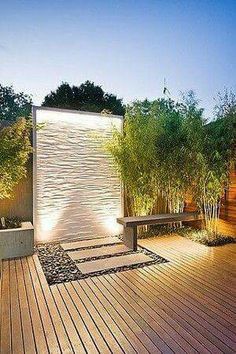 a wooden deck surrounded by plants and trees at night with lights shining on the wall