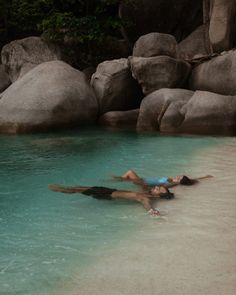 two people laying on their backs in the water next to some large rocks and boulders