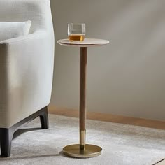 a small table with a glass on it in front of a white chair and rug