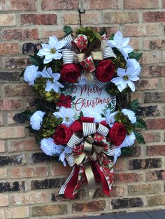 a christmas wreath hanging on the side of a brick wall with red and white flowers