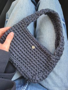 a person is holding a crocheted purse in their lap and wearing blue jeans