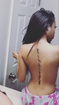 a woman with a tattoo on her back sitting in front of a bathroom door and looking at the mirror