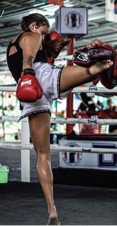 a woman kickboxing in a boxing ring with her leg on the punching bag