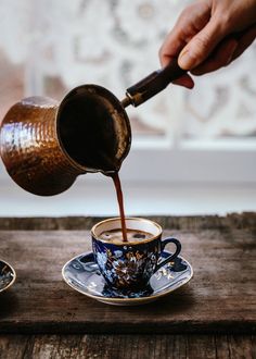 a person pours coffee from a teapot into two cups on a wooden table