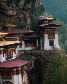 some white and red buildings on the side of a cliff with mountains in the background