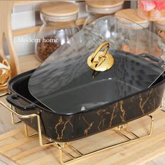 a black casserole dish with gold handles on a wooden tray