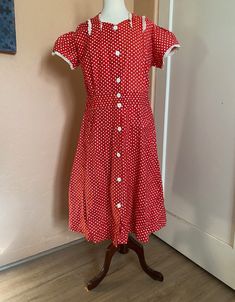 Charming 1940s era short-sleeved, red cotton dress with white polka dots. Abbreviated  sweetheart neckline and short puff sleeves trimmed with delicate, white cotton scalloped and ruffled eyelet trim. Front closure of white plastic buttons that feature an inlaid abstract floral design. Light fading on top of right sleeve (see photo). Researchers: this dress has loads of label info! Front of label reads "Pepsi=Coat Reg. Pend. Guaranteed Washable" - reverse side "Suburban Cottons, Inc." measurements: (taken flat and doubled and measured in inches) estimated size: L - XL bust: 44-45 inches waist: 36 inches hips: 46 inches shoulders: 16.5 inches shoulder to waist: 15 inches length: 42 inches size if marked: remnants of size tag, but unreadable To ensure a good fit, please compare measurements 1950s Short Sleeve Dress For Vintage Fashion, 1950s Short Sleeve Vintage Fashion Dress, 1950s Style Short Sleeve Vintage Dress, Retro Polka Dot Short Sleeve Dresses, 1950s Style Vintage Fashion Dress With Short Sleeves, Retro Short Sleeve Polka Dot Dress, Vintage Polka Dot Dress With Short Sleeves For Summer, 1950s Style Short Sleeve Lined Dress, 1950s Style Lined Short Sleeve Dresses