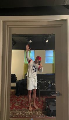 a man standing in front of a mirror with his hand up to the ceiling and wearing a red hat