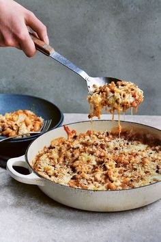 a person is spooning some food out of a skillet with another pan in the background