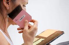 a woman is holding a brush to her face and looking at the makeup palette in front of her