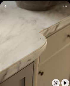 a white marble counter top next to a bowl on a cabinet in a room with other cabinets