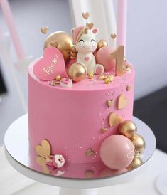 a pink cake decorated with gold hearts and a unicorn on top is sitting on a table