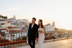 a bride and groom walking together in front of the cityscape at sunset or sunrise