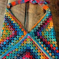 a multicolored crocheted bag hanging from a wooden table with wood planks