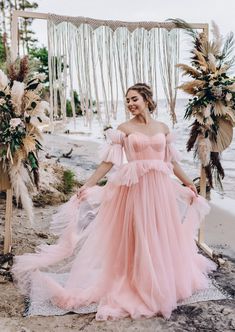 a woman in a pink dress is standing on the beach with her arms around her waist