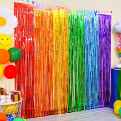 a rainbow colored party with balloons and streamers on the wall, along with other decorations