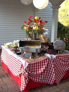 a table covered in red and white checkered cloths with food on the grill