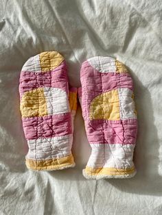 two oven mitts sitting on top of a bed covered in white and yellow material