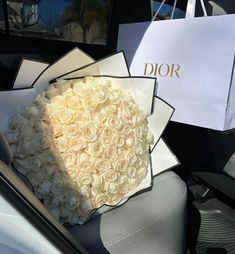 a bouquet of white roses sitting on top of a car seat in front of a dior bag