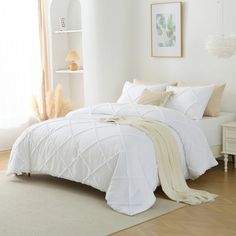 a bed with white comforter and pillows in a room next to a book shelf