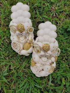 two pairs of white sandals with gold and pearls on them sitting in the grass next to each other