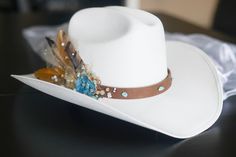 "Bridal Western Cowgirl Hat, ONE SIZE FITS ALL! It is a durable canvas material.  PLEASE NOTE THE BRIDAL VEIL IS NO LONGER AVAILABLE DUE TO LOW DEMAND. If you would like this feature added, please add \"bridal veil\" in the 'message seller' box before purchasing The leather strap has turquoise beads all around it, and on the right side there is a geode blue gem attached to the side, along with champagne (light and dark) colored beading, white beads (sparkly and plain white beading), gold colored tool with glitter embedded in the tool, and 3-4 feathers all attached by gorilla glue and hot glue. The hat also has a vinyl sticker attached to the right side of the hat to let everyone know you are the bride to be! There is an elastic strap on the inside of the hat to keep your head comfortable a Western Bride Hat, Bridal Cowgirl, Bride Cowgirl Hat, Womens Western Hats, Western Bride, Ivory Bride, Bridal Hat, Bohemian Bridal, Cowgirl Hat