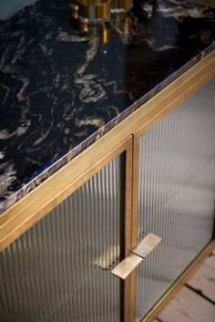 a black marble counter top next to a metal cabinet with glass doors and brass handles