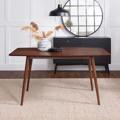 a wooden table sitting in front of a round mirror on top of a dresser next to a plant